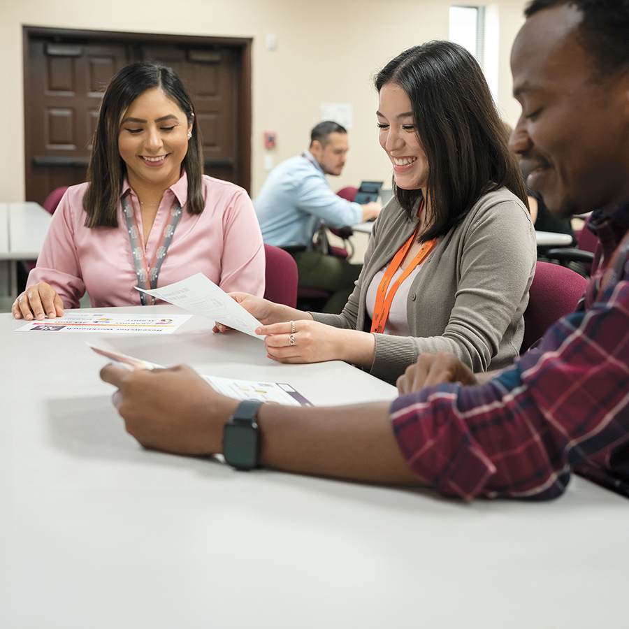 Three people sitting at a table together, looking at All of Us materials