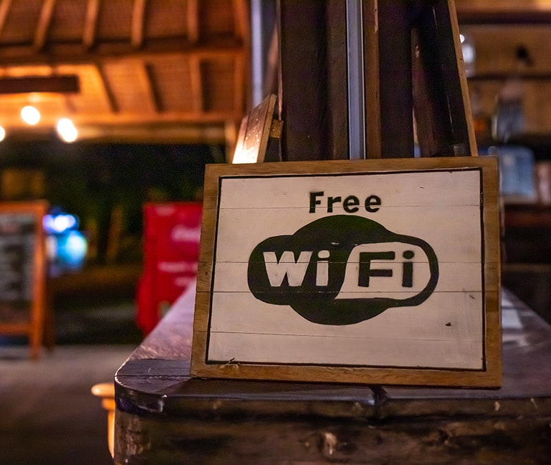 A 'Free Wi-Fi' sign at a cozy evening venue raises the question: is free wifi safe?