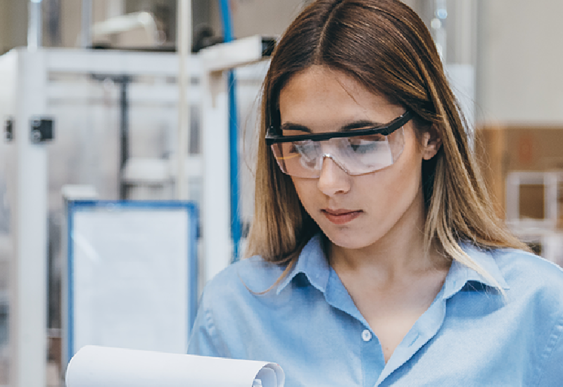 A young woman wearing protective goggles reads from a clipboard