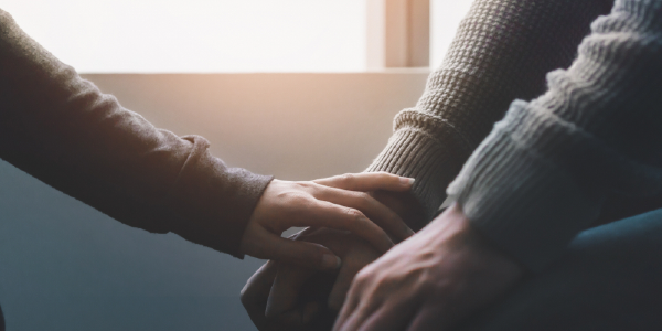 Close-up of a therapist reaching towards the hands of a patient in a comforting gesture.