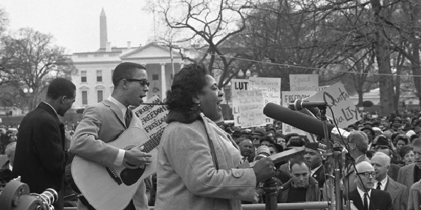 Fannie Lou Hamer singing at the microphones, with a guitarist, during a civil rights demonstration in front of the White House circa 1964. 