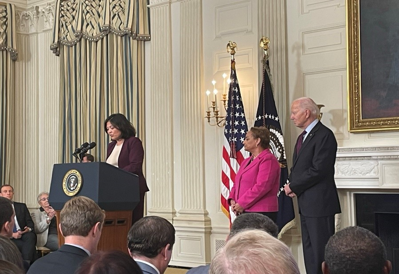 Acting Secretary of Labor Julie Su stands at a podium at the White House with President Joe Biden.