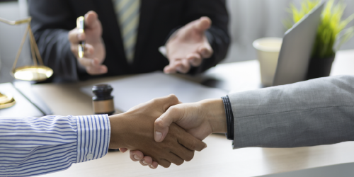 Two people shake hands at a table. A mediator is visible behind them.