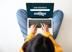 A woman types on a laptop open to a screen reading 'job search.'