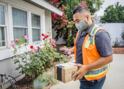 A male worker wearing a safety vest delivers a package to a home