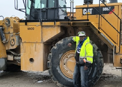 A construction worker with a hard hat stands in front of a large construction vehicle.