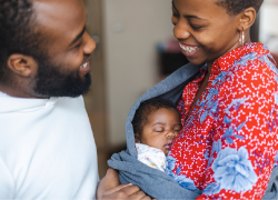 A happy family: A man and a woman cradling a baby in a sling.