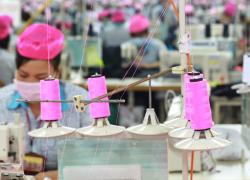 A garment worker at a Better Work factory in Vietnam. Spools of pink thread are visible in the foreground. Credit: Better Work.