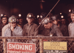 A sepia-toned photograph of miners in the 1970s in an elevator, about to descend into the mine to start their shift.