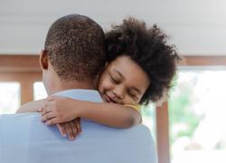 A child with curly hair hugging his dad around the neck.