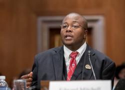 Edward Mitchell in a suit speaking into a microphone.