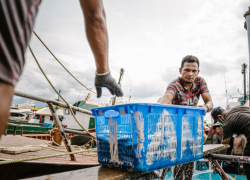 Fishers handling a large blue crate on a dock in Thailand.