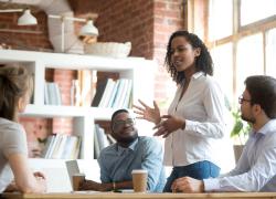 Female employee standing and speaking to seated colleagues