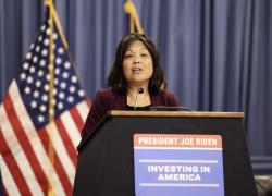 Acting Secretary Julie Su speaks at the Department of Labor's "Good Jobs, Great Cities Academy" launch event. She is standing behind a podium with a sign that says "President Joe Biden: Investing in America."