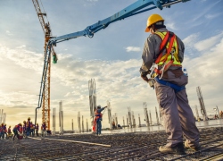 A construction worker in safety gear stands beneath a crane on a construction site.