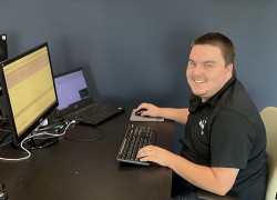 A young man working on a computer pauses to smile at the camera.