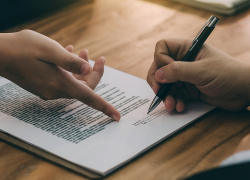 A worker signs an employment contract while the employer points to the signature area.