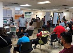 A man delivers a presentation to a group of people at the Mexican Consulate. A banner with information about EMPLEO is behind him.