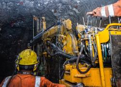 Miners are working in an underground mine under a roof supported with a mesh screen. 