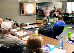 2022 TRAM attendees participate in a workshop on the gamification of safety and health training. The trainers sit around tables in a classroom, writing in notepads.