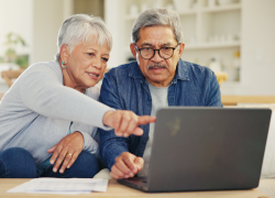 A senior couple sitting and looking at a laptop with documents next to it on a table.