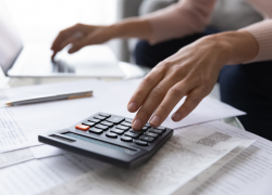 Close up photo of a woman's hands as she reviews retirement planning papers with her computer and calculator nearby