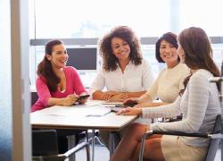 A diverse group of professional women gathered around a conference table. 