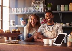 Two coffeeshop workers leaning on the counter and smiling. 