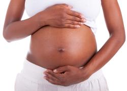 A pregnant Black woman holding her stomach.