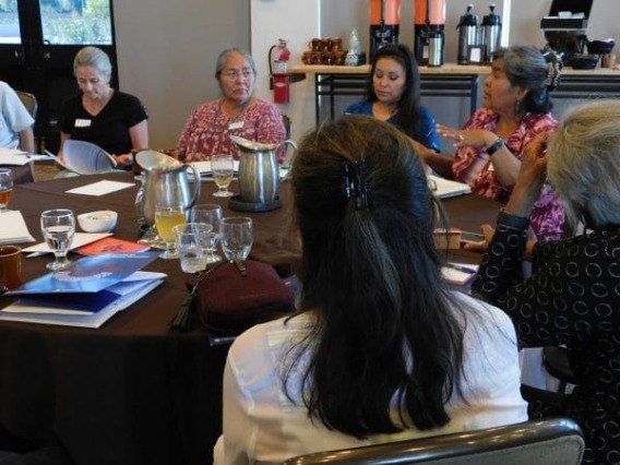 Six people sit at a table focused on one speaker.