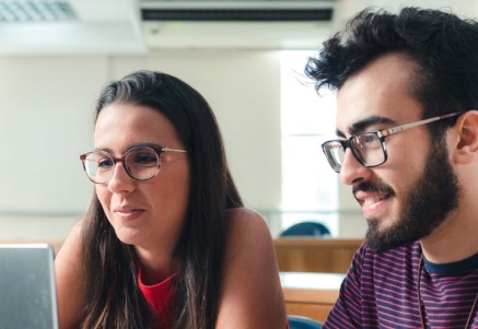 Imagem de dois jovens adultos uma mulher e um homem, olhando a tela de um laptop