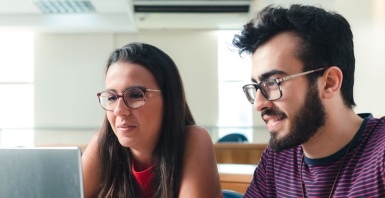 Imagem de dois jovens adultos uma mulher e um homem, olhando a tela de um laptop