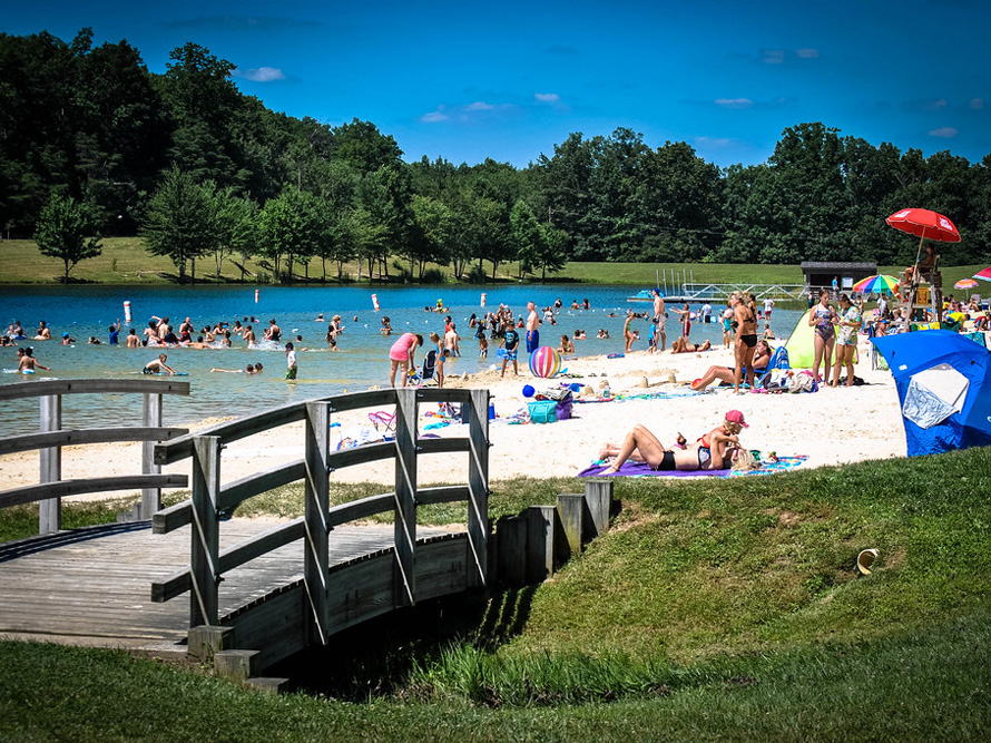 Beach by the lake, white sand, lifeguard and swimming area surrounded by mountains and forests