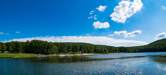 Beach from the lake, nessled in green trees and framed by a bright blue sky