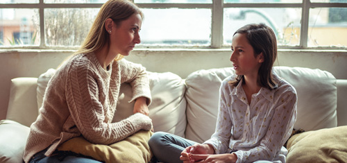 Mother and teen daughter sitting on a couch having a serious discussion