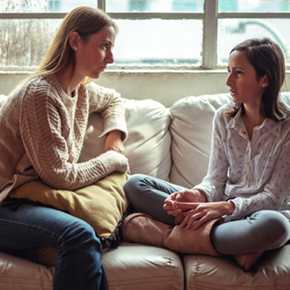 Mother and teen daughter sitting on a couch having a serious discussion