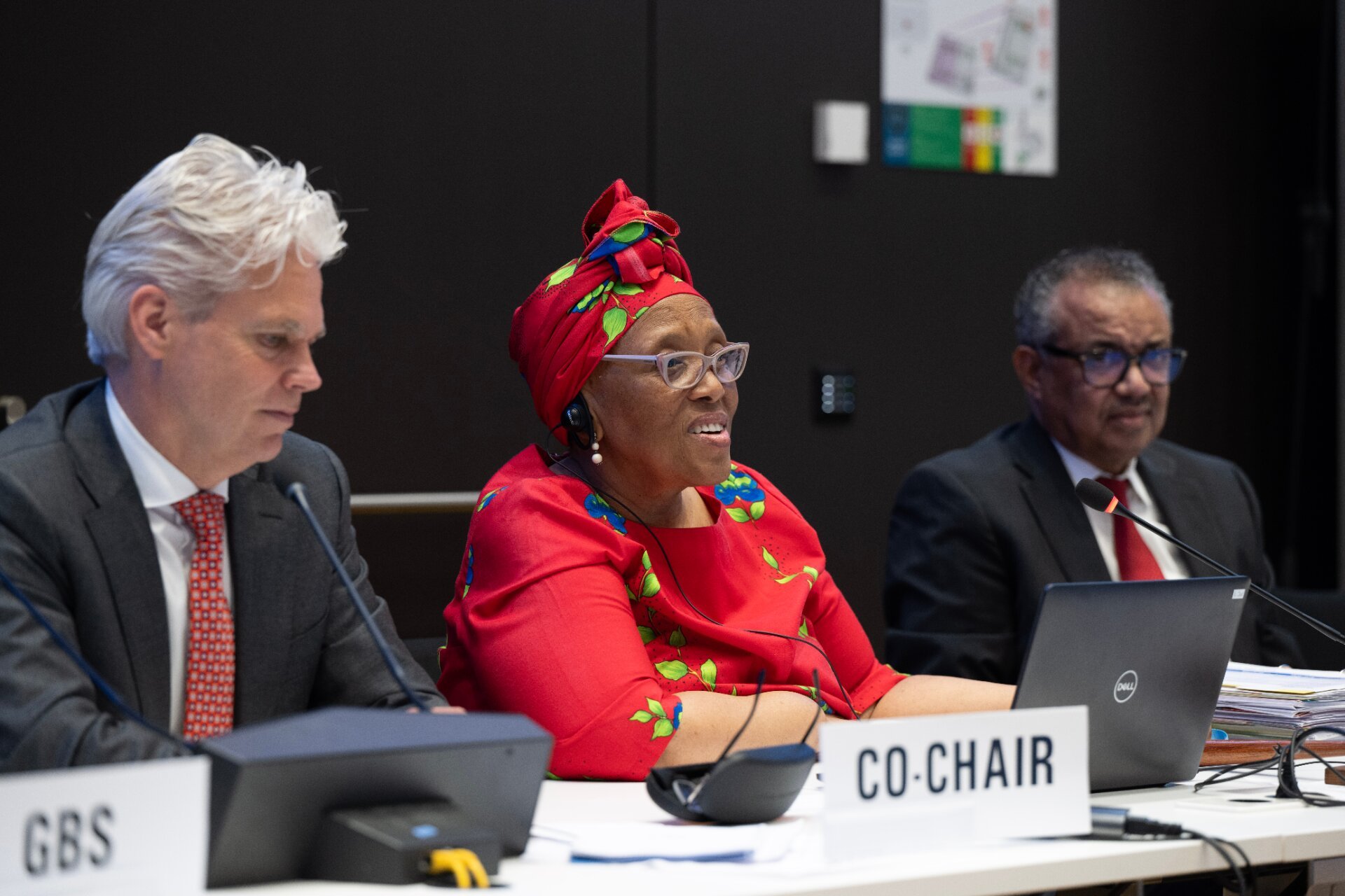 Two men in suits and one woman in African attire at a meeting.