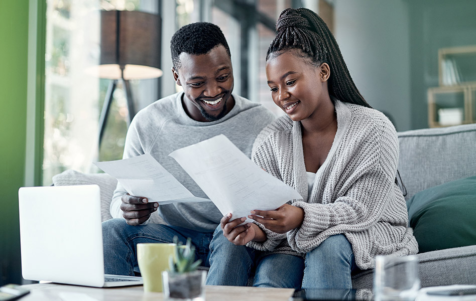 A couple sitting on a couch smile as they read a letter together