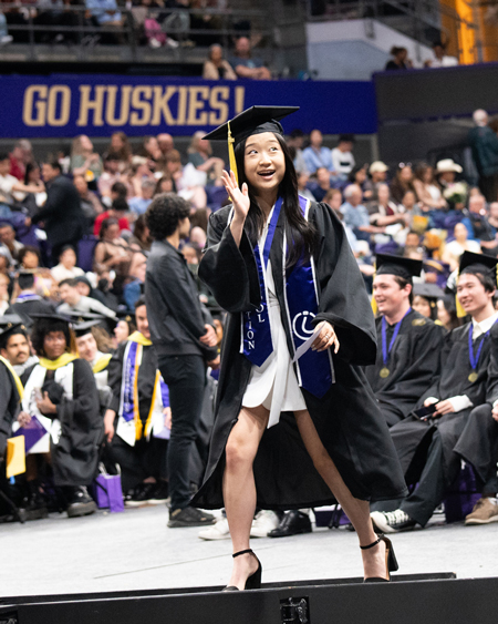 A woman waves as she walks toward the stage.