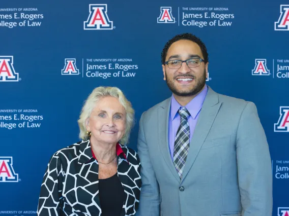 Two alumni, one older woman and one younger man, pose together for a photo.