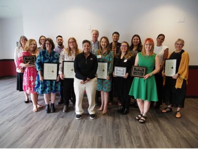 A large group of professionals smiles for the camera as they hold their awards.