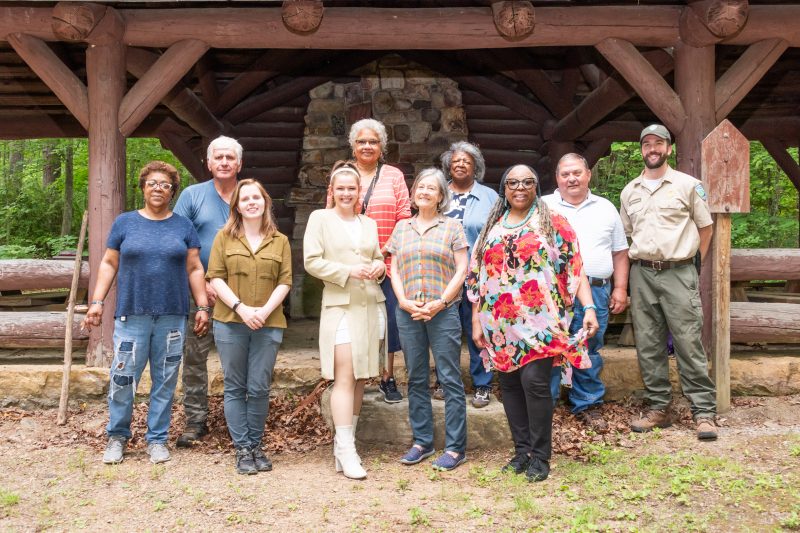 About 10 members of the project and partners stand together for a picture beneath a wooden structure