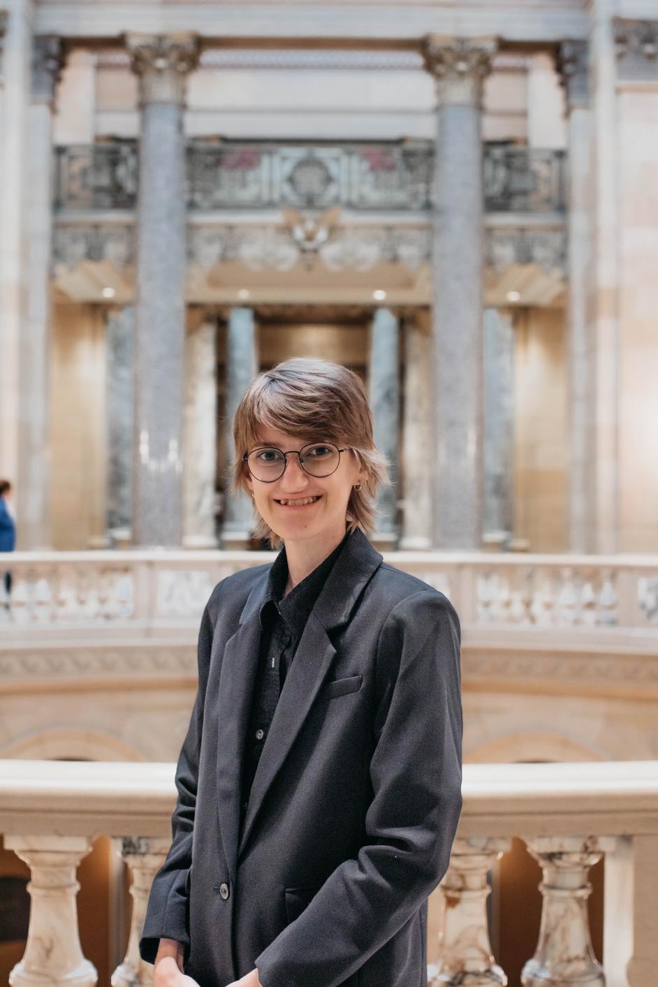 Riss, a white nonbinary person, wearing a black business jacket in the Capitol