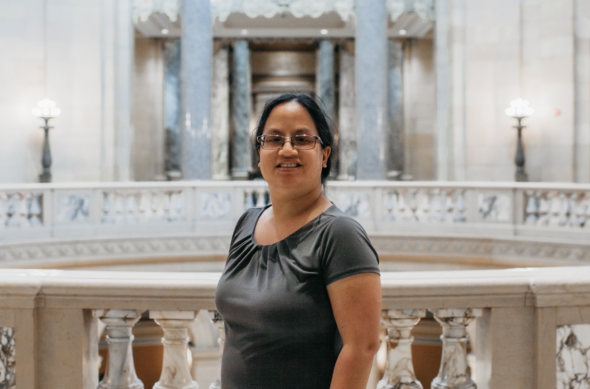 Liz, an Asian woman with pulled back hair, smiling and standing inside the Minnesota State Capitol