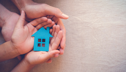 Two sets of hands nestled into one another holding an image of a house