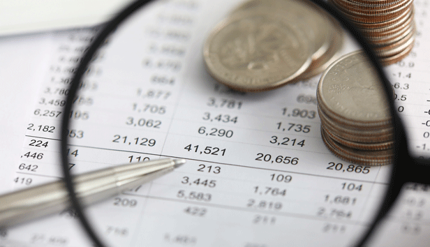 A magnifying glass against financial figures and stacks of coins