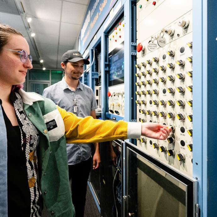 Scientist reaches out to flip a switch on a board with a colleague visible further away