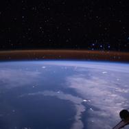 Photograph taken from space of the Earth with a thin orange shell just visible as the atmosphere; part of a spacecraft is visible to the side