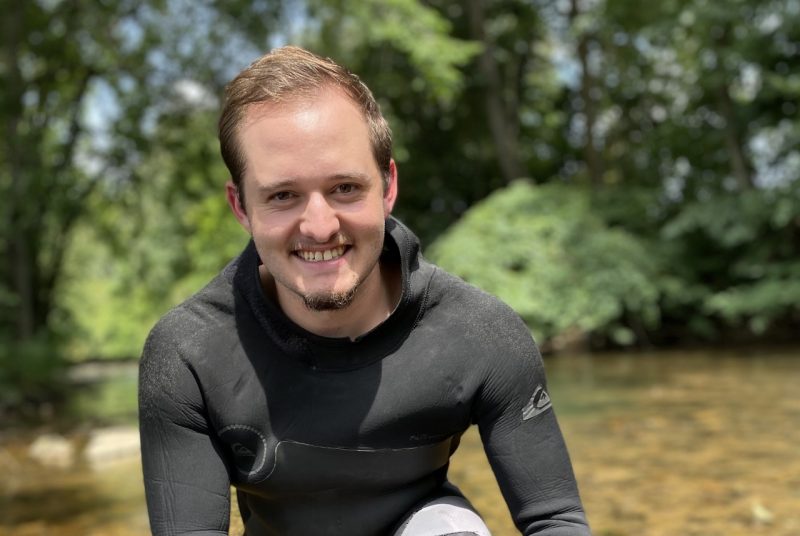 A person in a wetsuit stands in a stream.