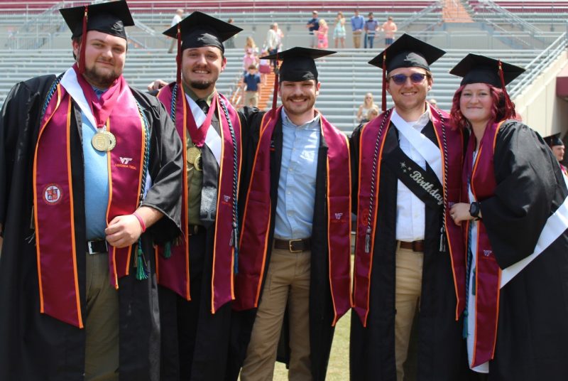 Five people in graduation robes stand in a row.